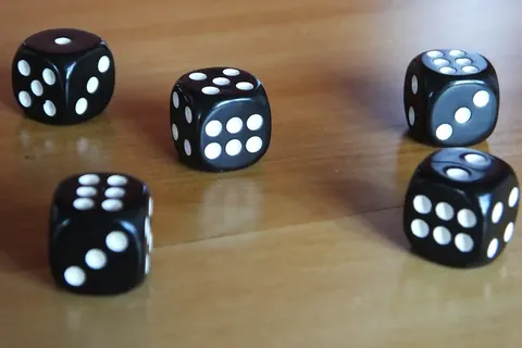 Five black dice scattered on a wooden surface